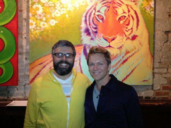 Pair standing before vibrant tiger portrait.