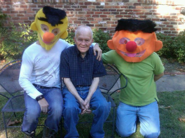 Elderly man flanked by costumed friends.