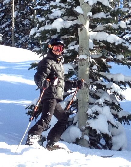 Person skiing beside snow-laden pine tree.