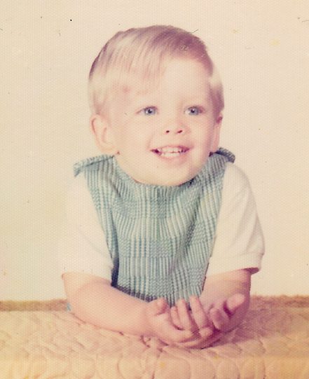 Smiling toddler in striped overalls, vintage photo.
