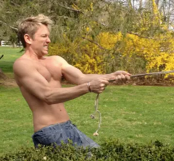 Man pulling a rope outdoors, shirtless.