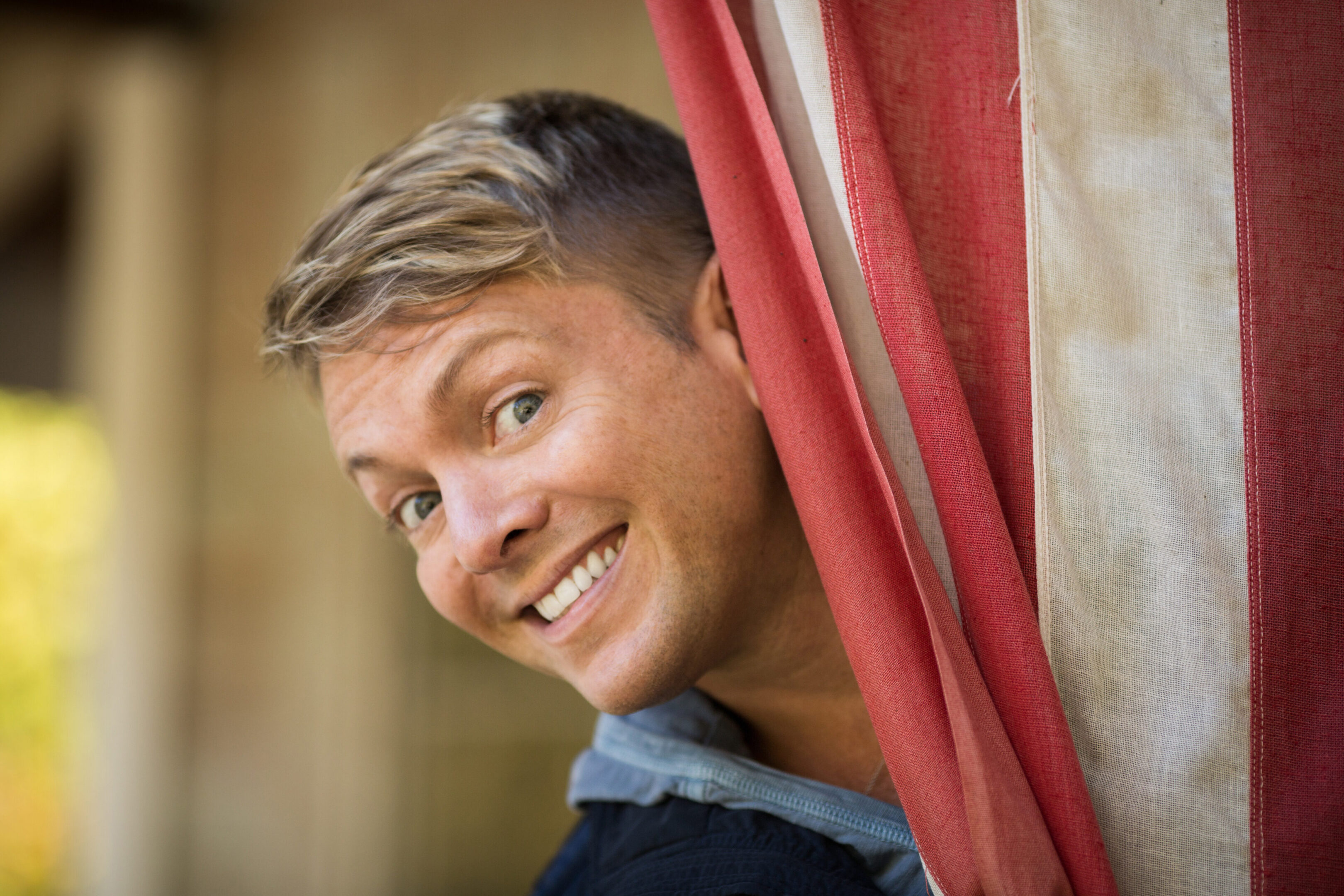 Smiling person peeking out from red curtain.