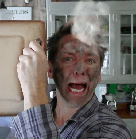 Man with soot-covered face holding pan.