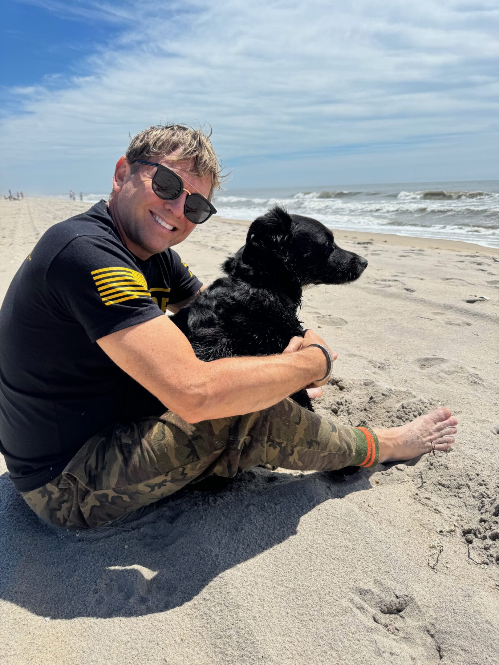 Man with dog sitting on sandy beach.