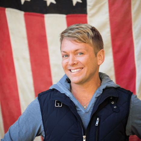 Man smiling in front of American flag.