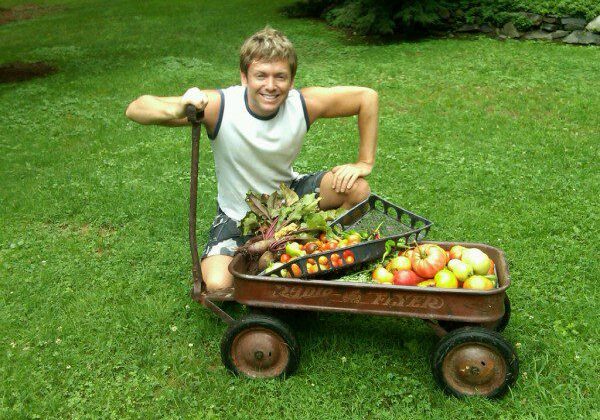 Smiling man kneeling by vegetable-filled wagon