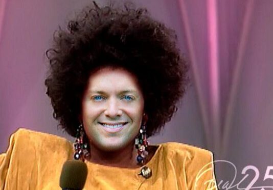 Individual with big hair and colorful earrings.